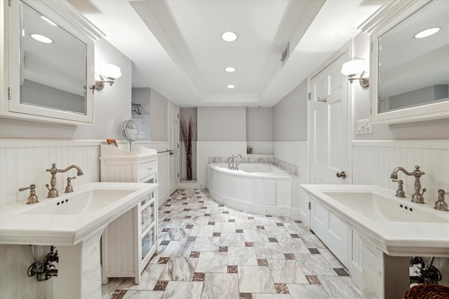 bathroom with a tray ceiling, double sink, and a bath