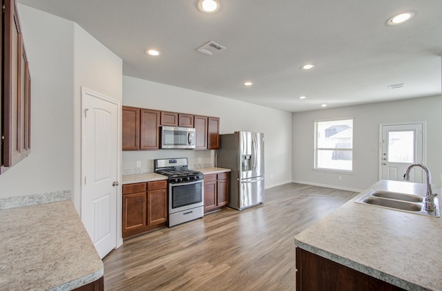 kitchen with wood-type flooring, stainless steel appliances, a kitchen island with sink, and sink