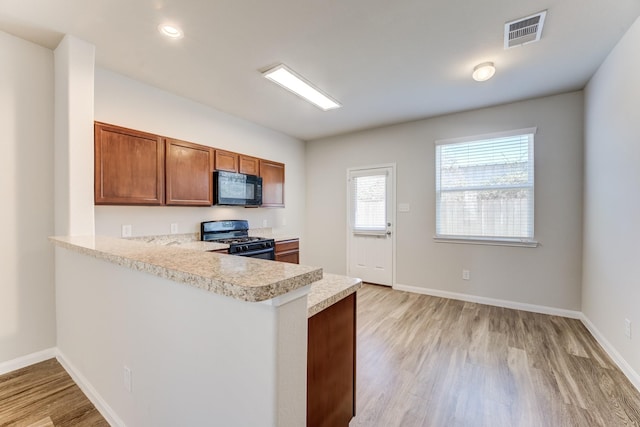 kitchen featuring light wood-type flooring, kitchen peninsula, and black appliances