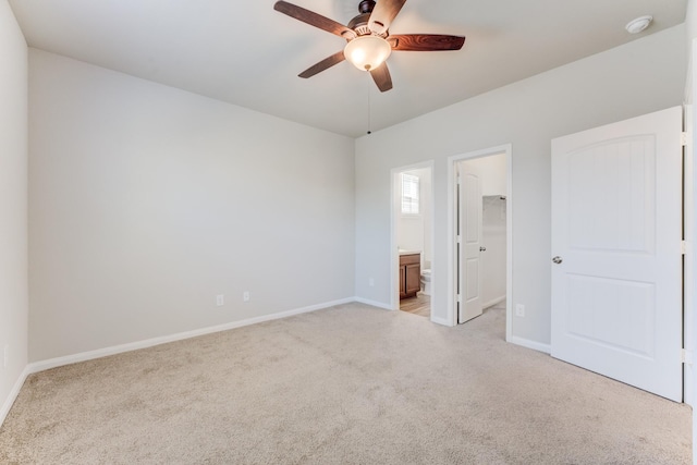 unfurnished bedroom with light colored carpet, a walk in closet, a closet, ceiling fan, and ensuite bathroom