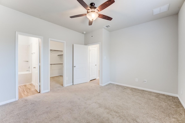 unfurnished bedroom featuring light carpet, ensuite bathroom, a walk in closet, and a closet