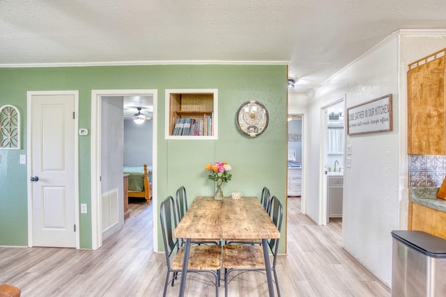 dining area featuring light hardwood / wood-style flooring, sink, crown molding, and a textured ceiling