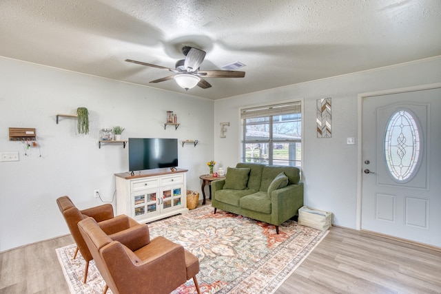 living room with a textured ceiling, crown molding, ceiling fan, and light hardwood / wood-style flooring