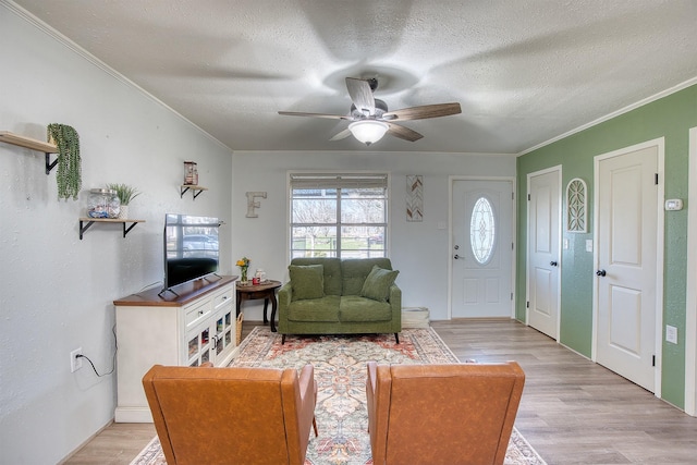 living room featuring light wood-type flooring, crown molding, a textured ceiling, and ceiling fan