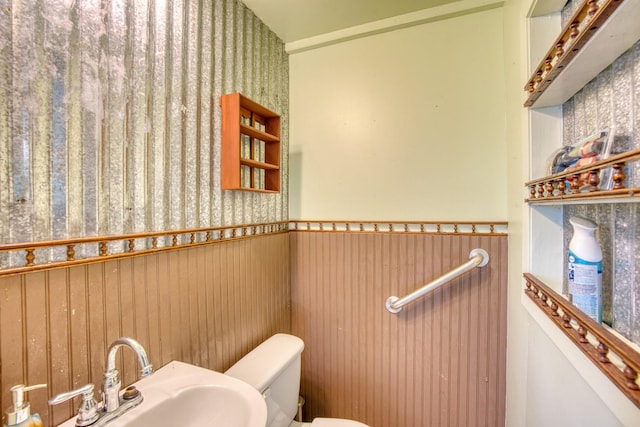 bathroom with sink, toilet, and wooden walls