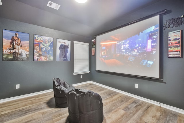 cinema room featuring baseboards, vaulted ceiling, wood finished floors, and visible vents