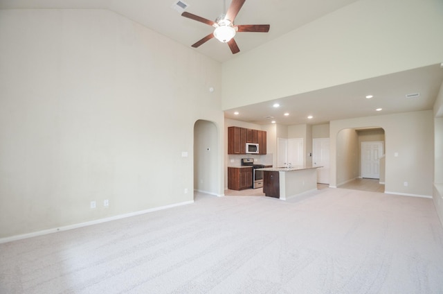 unfurnished living room with ceiling fan, sink, high vaulted ceiling, and light colored carpet