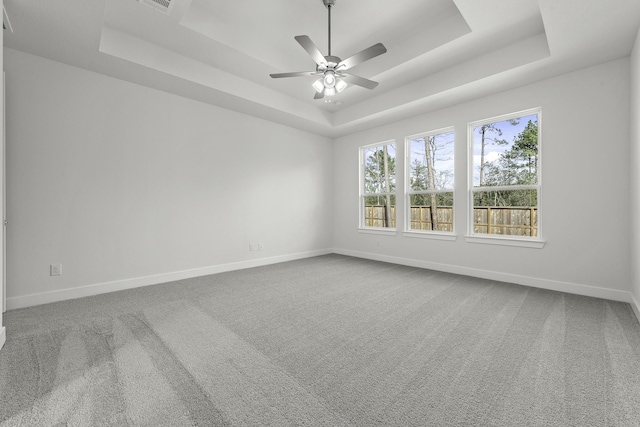 empty room with a tray ceiling, ceiling fan, and carpet flooring