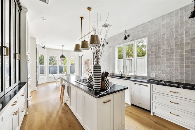 kitchen featuring appliances with stainless steel finishes, light wood-type flooring, pendant lighting, sink, and white cabinetry