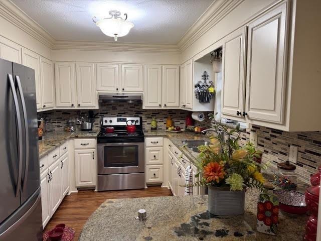 kitchen with white cabinetry, dark hardwood / wood-style flooring, stone counters, appliances with stainless steel finishes, and crown molding