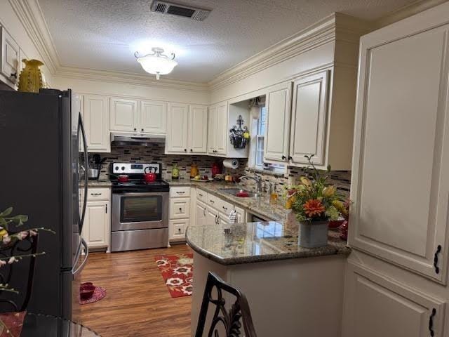 kitchen with hardwood / wood-style floors, sink, stainless steel appliances, kitchen peninsula, and white cabinets