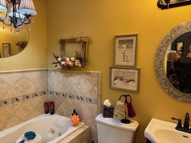 bathroom with tiled bath, toilet, sink, and a notable chandelier