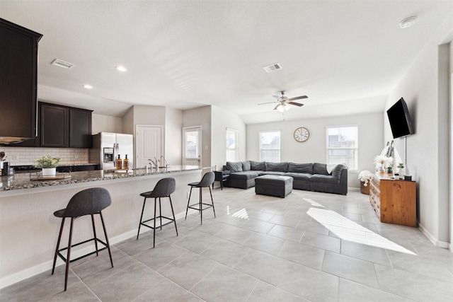 kitchen featuring a breakfast bar, visible vents, open floor plan, stainless steel fridge with ice dispenser, and dark stone countertops