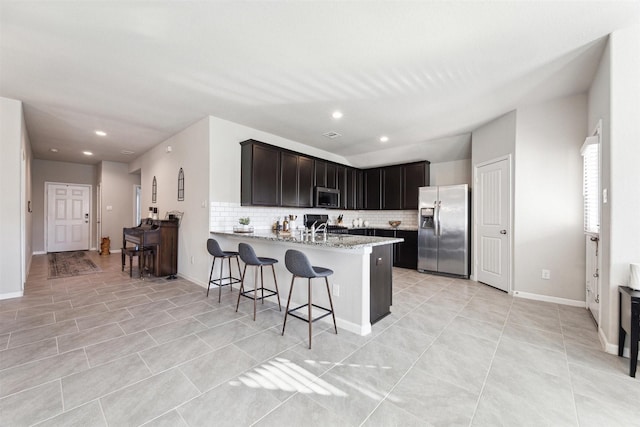 kitchen with appliances with stainless steel finishes, a sink, decorative backsplash, and light stone countertops