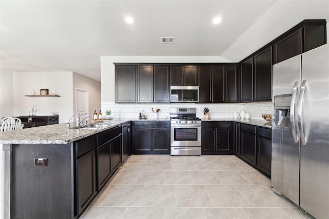 kitchen with light stone counters, stainless steel appliances, visible vents, a sink, and a peninsula