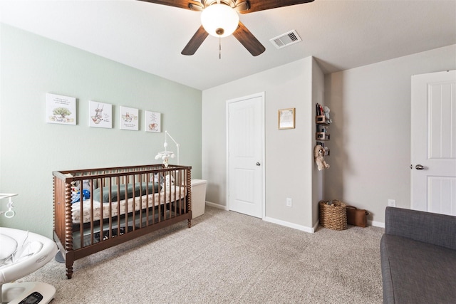 bedroom with light colored carpet, visible vents, ceiling fan, a crib, and baseboards