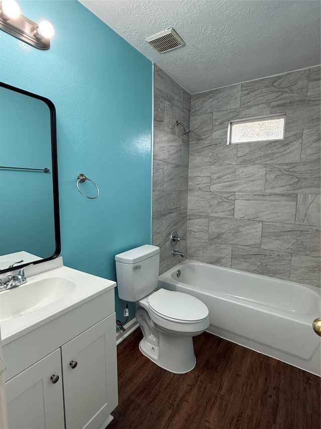 full bathroom with wood-type flooring, vanity, a textured ceiling, tiled shower / bath, and toilet