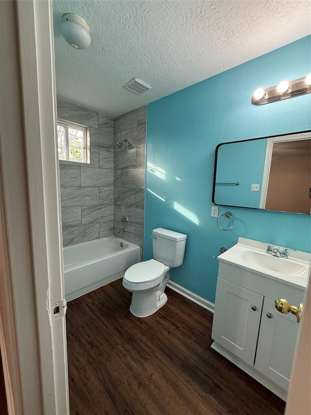 full bathroom featuring tiled shower / bath combo, toilet, wood-type flooring, a textured ceiling, and vanity