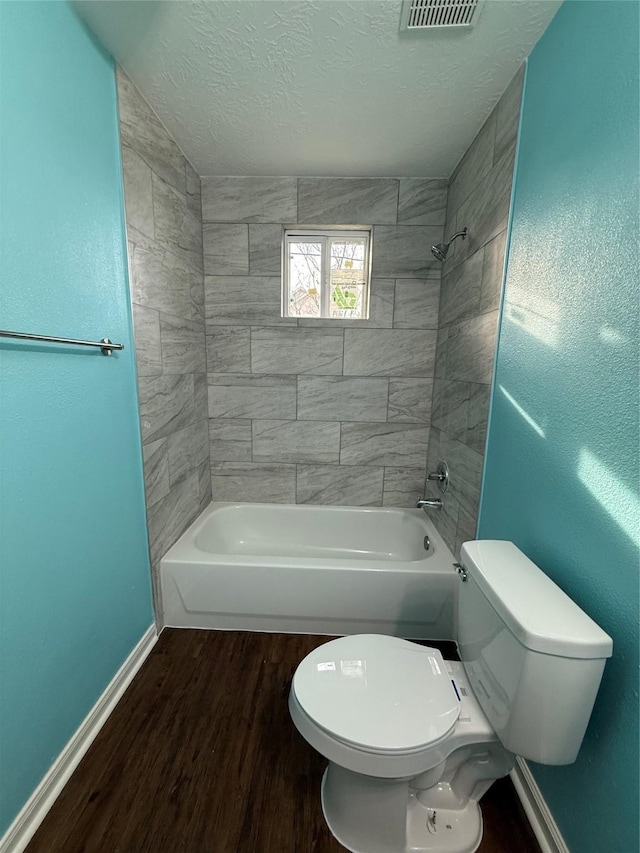 bathroom featuring tiled shower / bath, toilet, a textured ceiling, and hardwood / wood-style floors