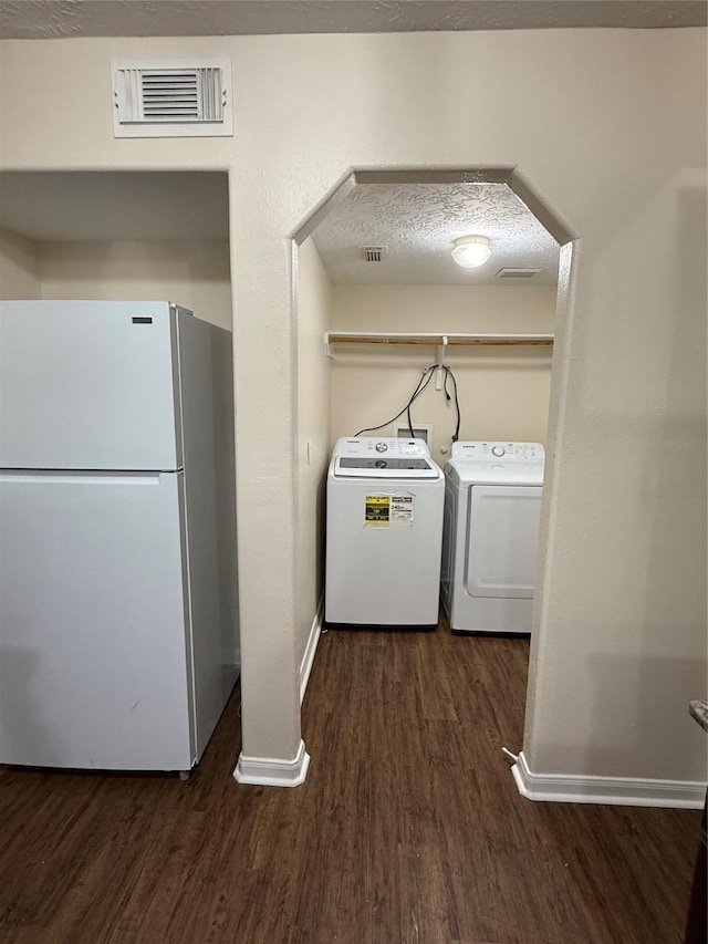 clothes washing area with a textured ceiling, washing machine and clothes dryer, and dark hardwood / wood-style flooring