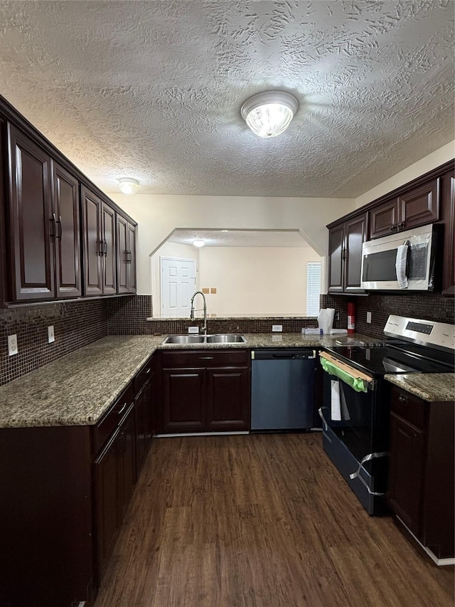 kitchen with dark brown cabinets, stainless steel appliances, light stone countertops, sink, and dark hardwood / wood-style floors