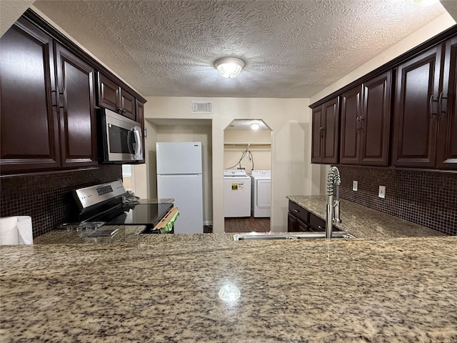 kitchen with appliances with stainless steel finishes, washer and dryer, backsplash, light stone counters, and sink