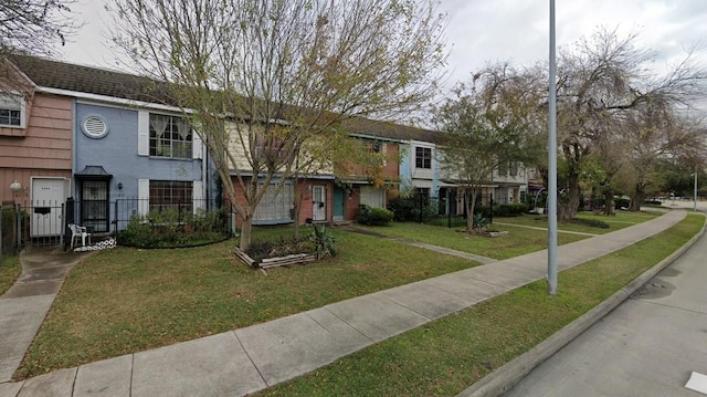 multi unit property with brick siding, a front yard, and fence