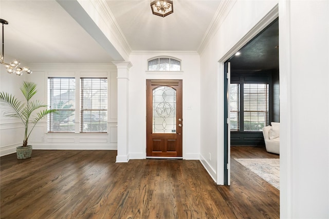 entrance foyer featuring decorative columns, ornamental molding, dark hardwood / wood-style floors, and a notable chandelier