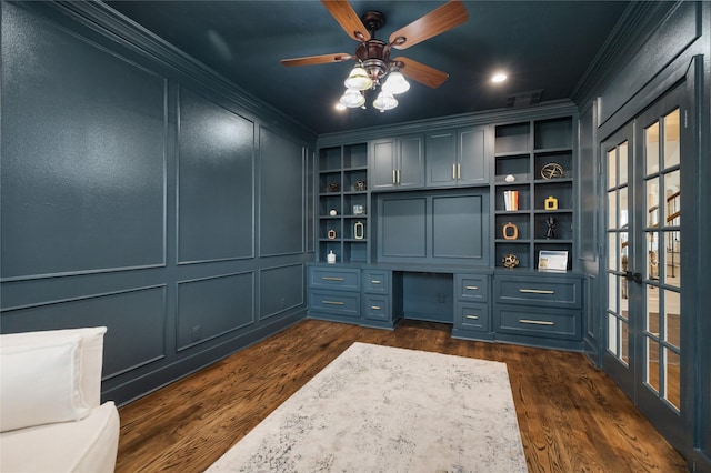 unfurnished office featuring built in desk, built in shelves, ceiling fan, crown molding, and dark hardwood / wood-style floors