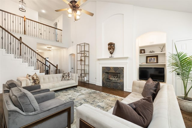 living room featuring a towering ceiling, ceiling fan, a fireplace, dark hardwood / wood-style floors, and built in features