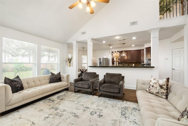 living room featuring ceiling fan, light wood-type flooring, high vaulted ceiling, and ornate columns