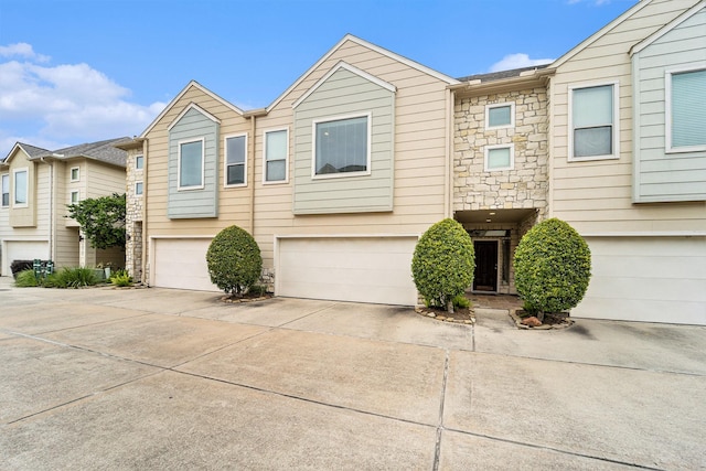 townhome / multi-family property with stone siding, driveway, and an attached garage