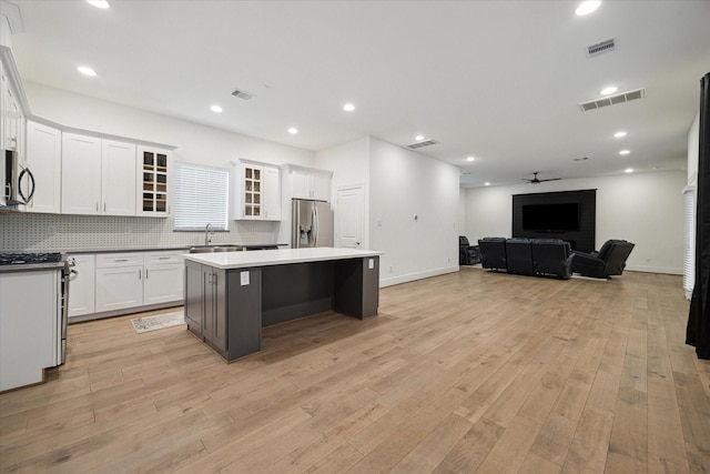 kitchen with appliances with stainless steel finishes, tasteful backsplash, a center island, light wood-type flooring, and white cabinetry