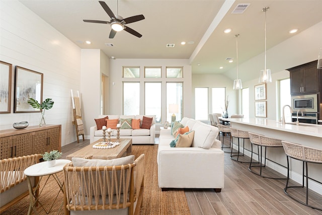 living room featuring light wood-type flooring, sink, wood walls, and plenty of natural light