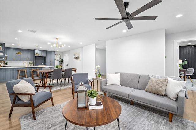 living room featuring ceiling fan with notable chandelier and light hardwood / wood-style flooring