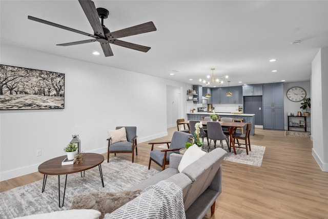 living room with ceiling fan with notable chandelier and light hardwood / wood-style flooring