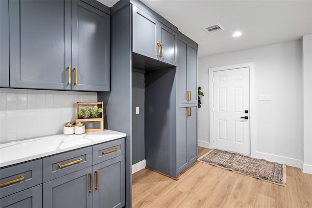 kitchen featuring decorative backsplash, light wood-type flooring, light stone counters, and gray cabinetry