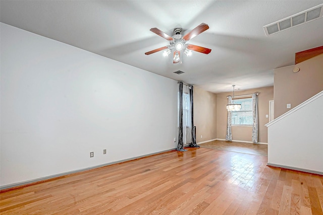 spare room with ceiling fan with notable chandelier and light wood-type flooring