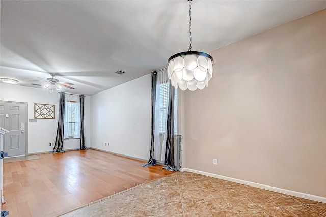 unfurnished living room with ceiling fan with notable chandelier and light hardwood / wood-style flooring