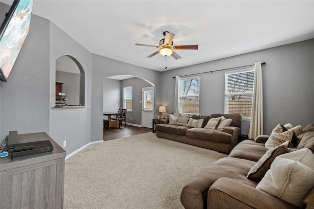 living room featuring baseboards, arched walkways, dark colored carpet, and a ceiling fan