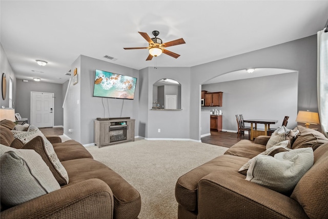 carpeted living room with arched walkways, visible vents, ceiling fan, and baseboards