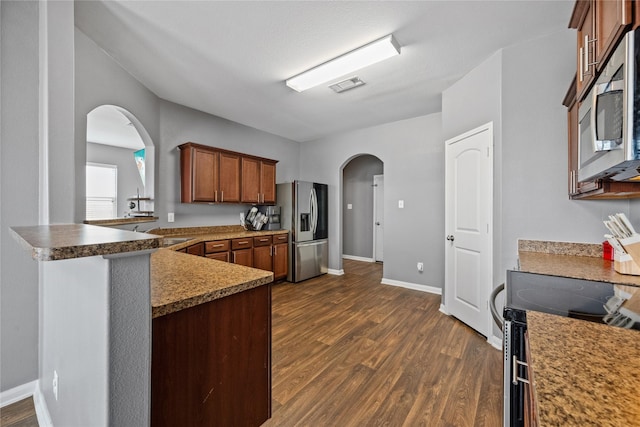 kitchen featuring visible vents, brown cabinetry, arched walkways, dark countertops, and appliances with stainless steel finishes