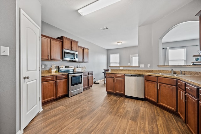 kitchen featuring dark wood-style flooring, stainless steel appliances, visible vents, brown cabinetry, and a sink