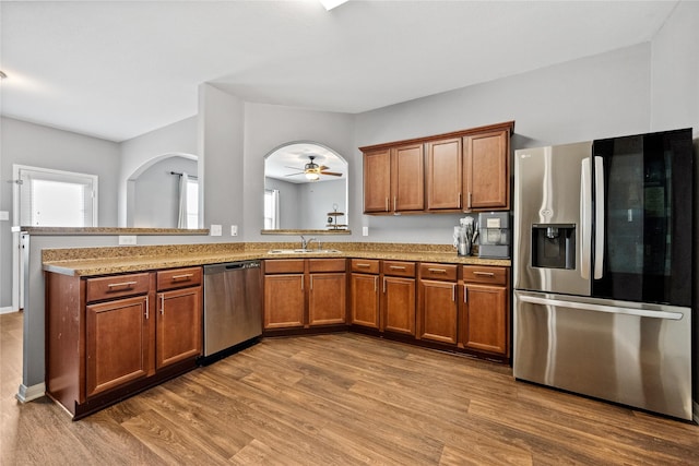 kitchen featuring light stone counters, wood finished floors, a sink, appliances with stainless steel finishes, and brown cabinetry