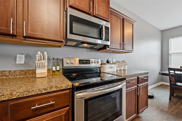 kitchen featuring dark wood-style flooring, stainless steel appliances, stone countertops, brown cabinetry, and baseboards