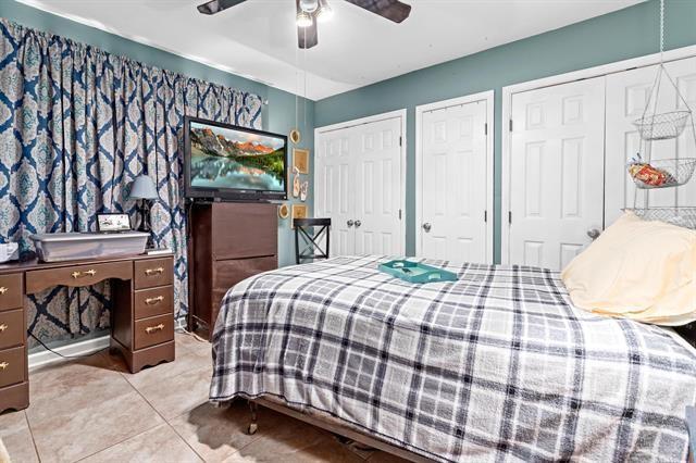 bedroom featuring light tile patterned flooring, ceiling fan, and two closets