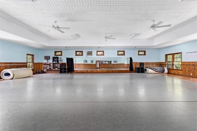 miscellaneous room featuring a tray ceiling, wooden walls, ceiling fan, and concrete floors