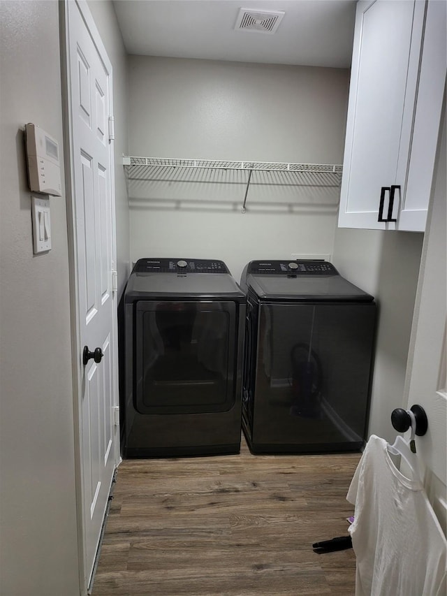 clothes washing area featuring hardwood / wood-style flooring, washing machine and dryer, and cabinets