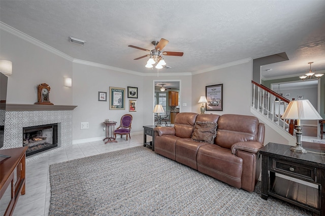 tiled living room featuring ceiling fan, a fireplace, a textured ceiling, and ornamental molding