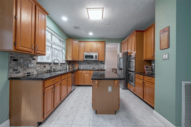 kitchen with stainless steel appliances, dark stone counters, decorative backsplash, a kitchen island, and sink